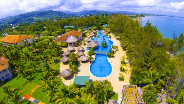 A resort with a large swimming pool, palm trees, and a view of the ocean. - La Ensenada Beach Resort - All Inclusive (Tela)