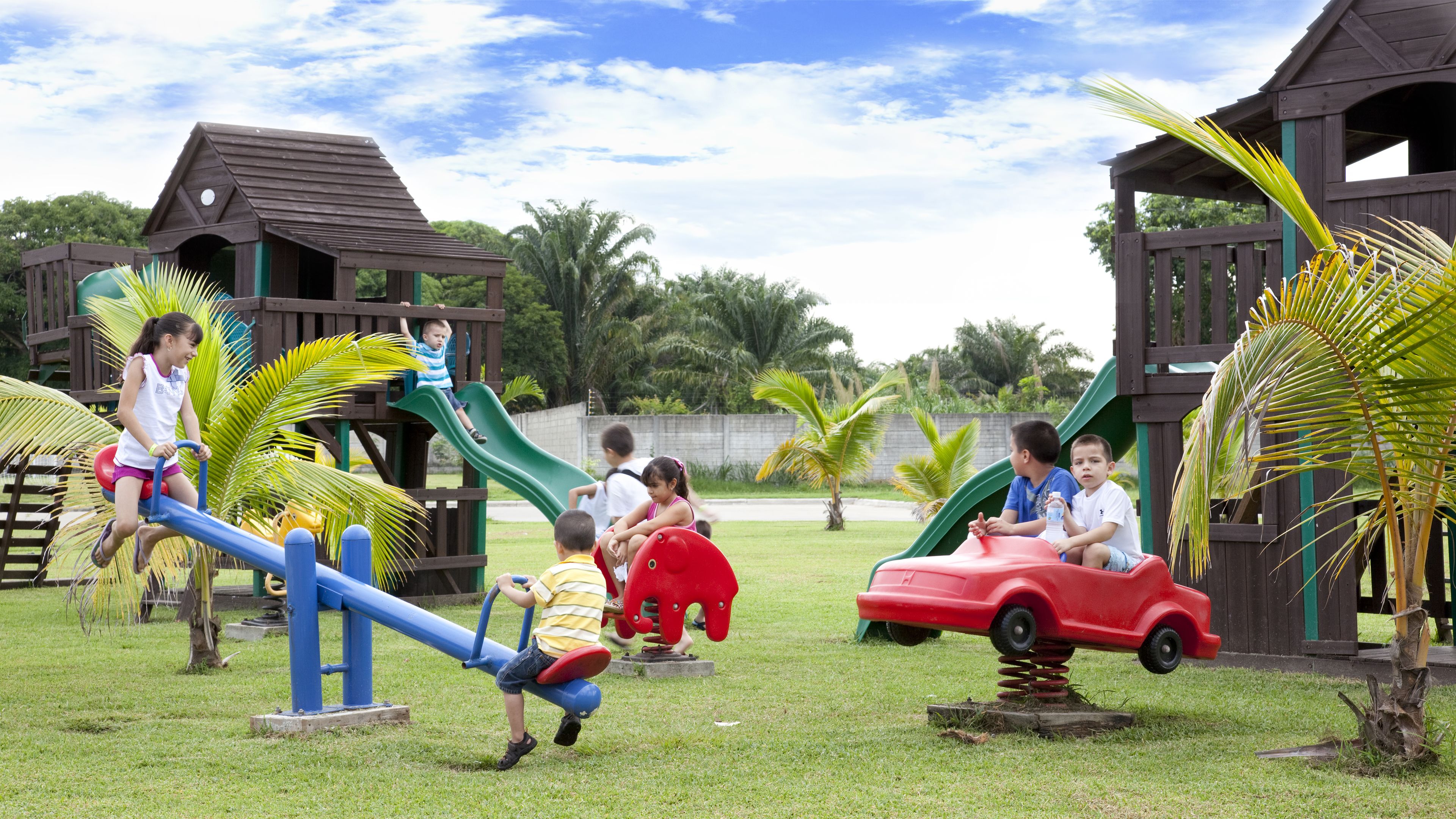 Un parque infantil con sube y bajas, un tobogán y un coche de juguete rojo.
