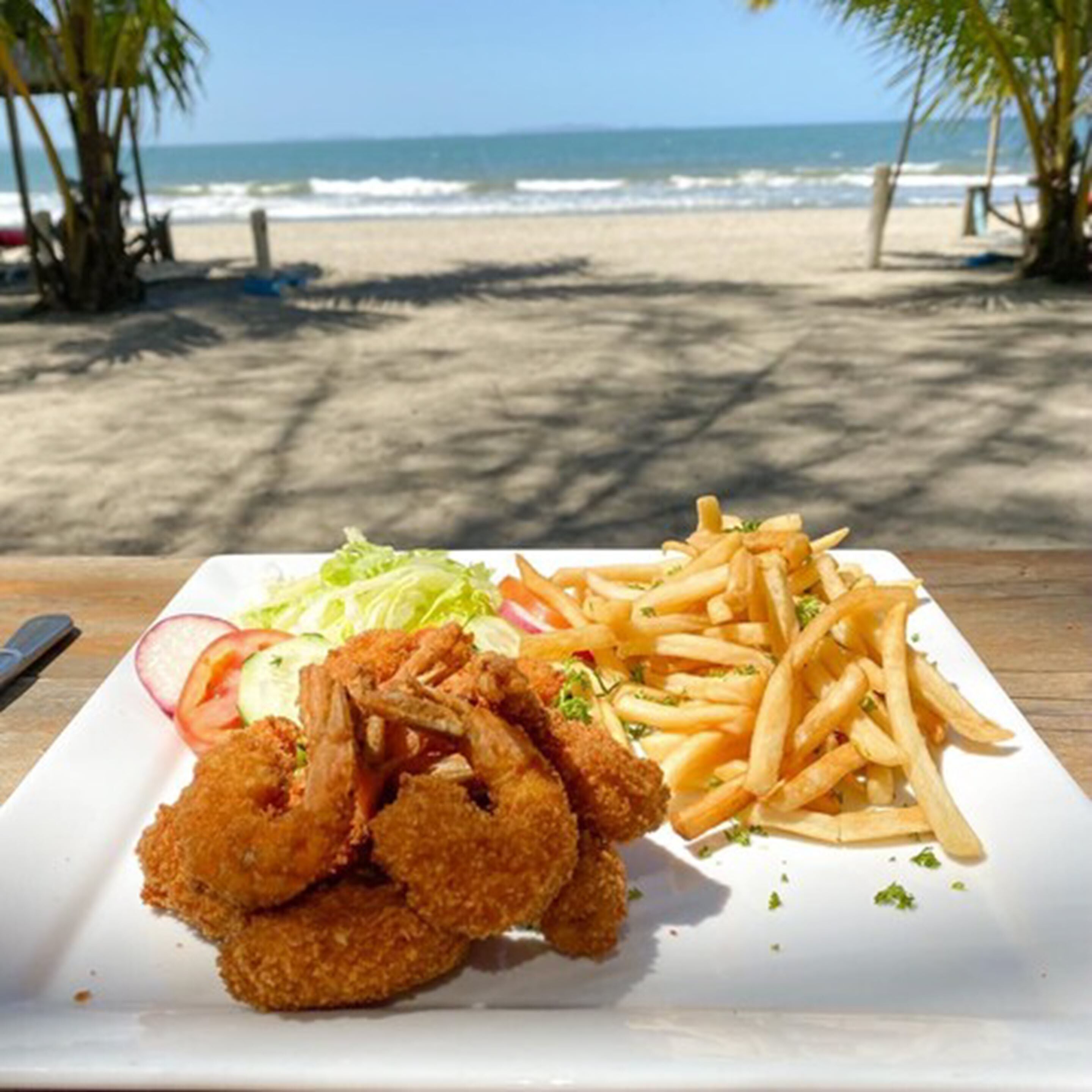 A plate of food with fried items and fries on a beach.