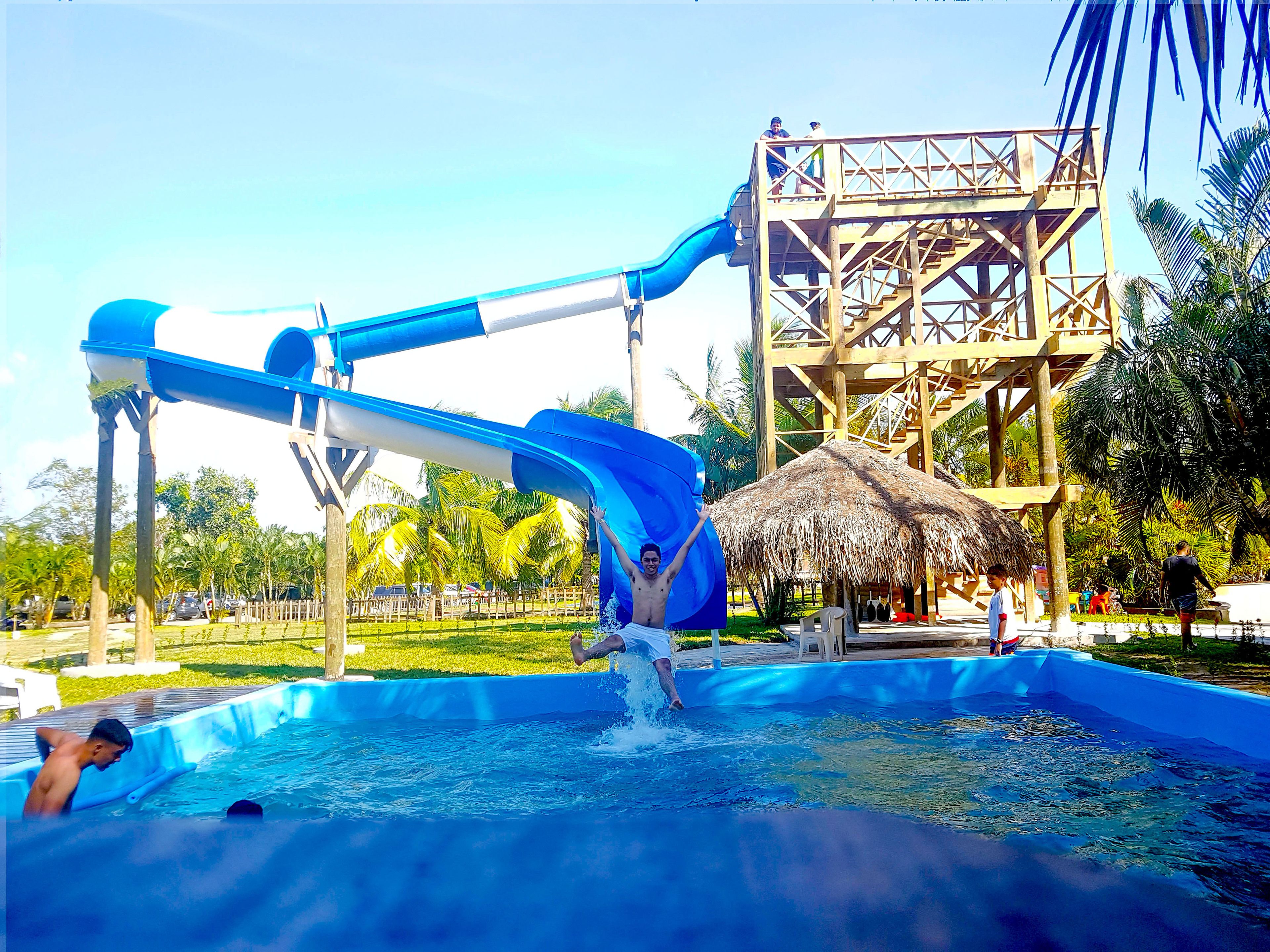 Parque acuático con un tobogán de agua azul, una piscina y una estructura de techo de paja.