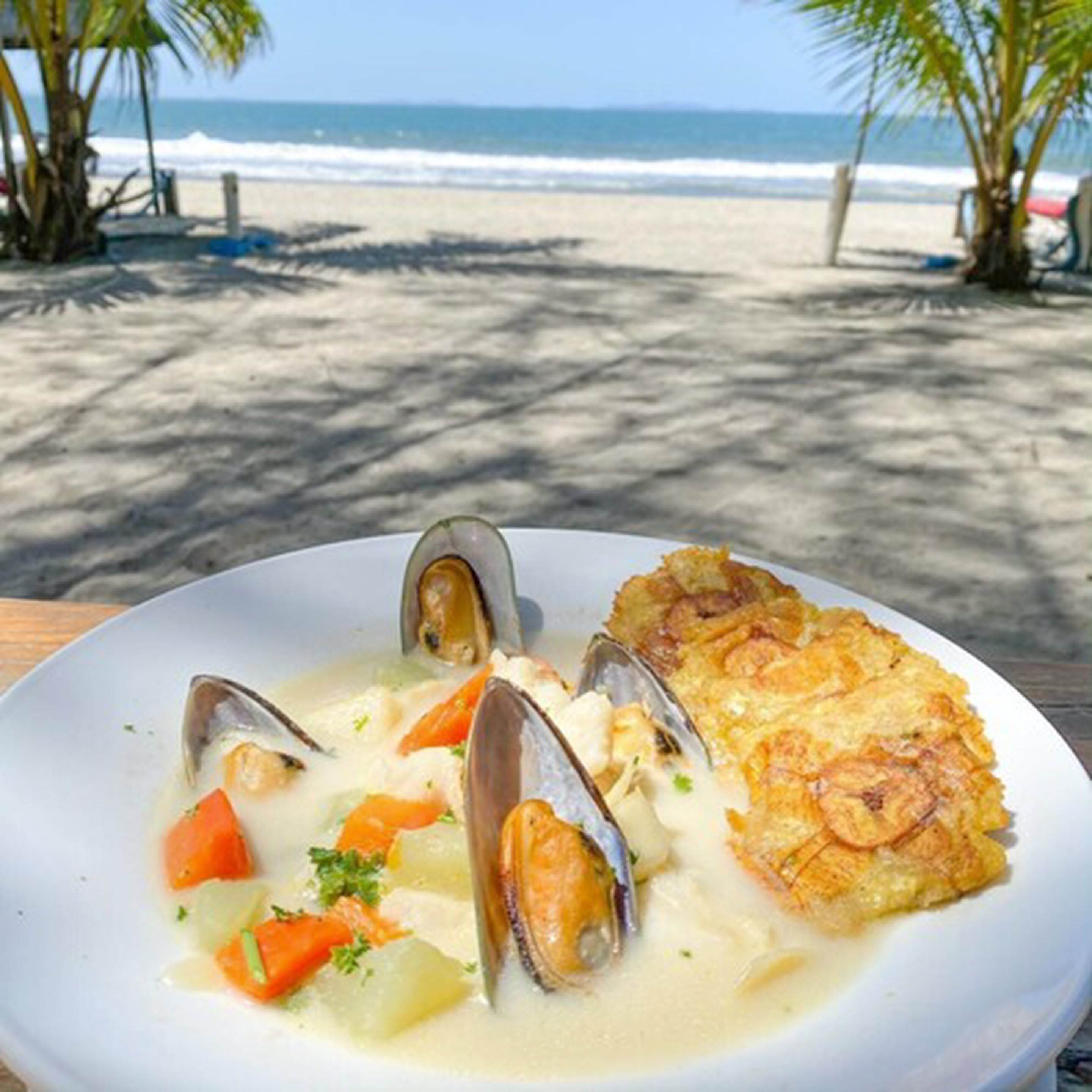A seafood dish on a white plate with a beach and palm trees in the background.