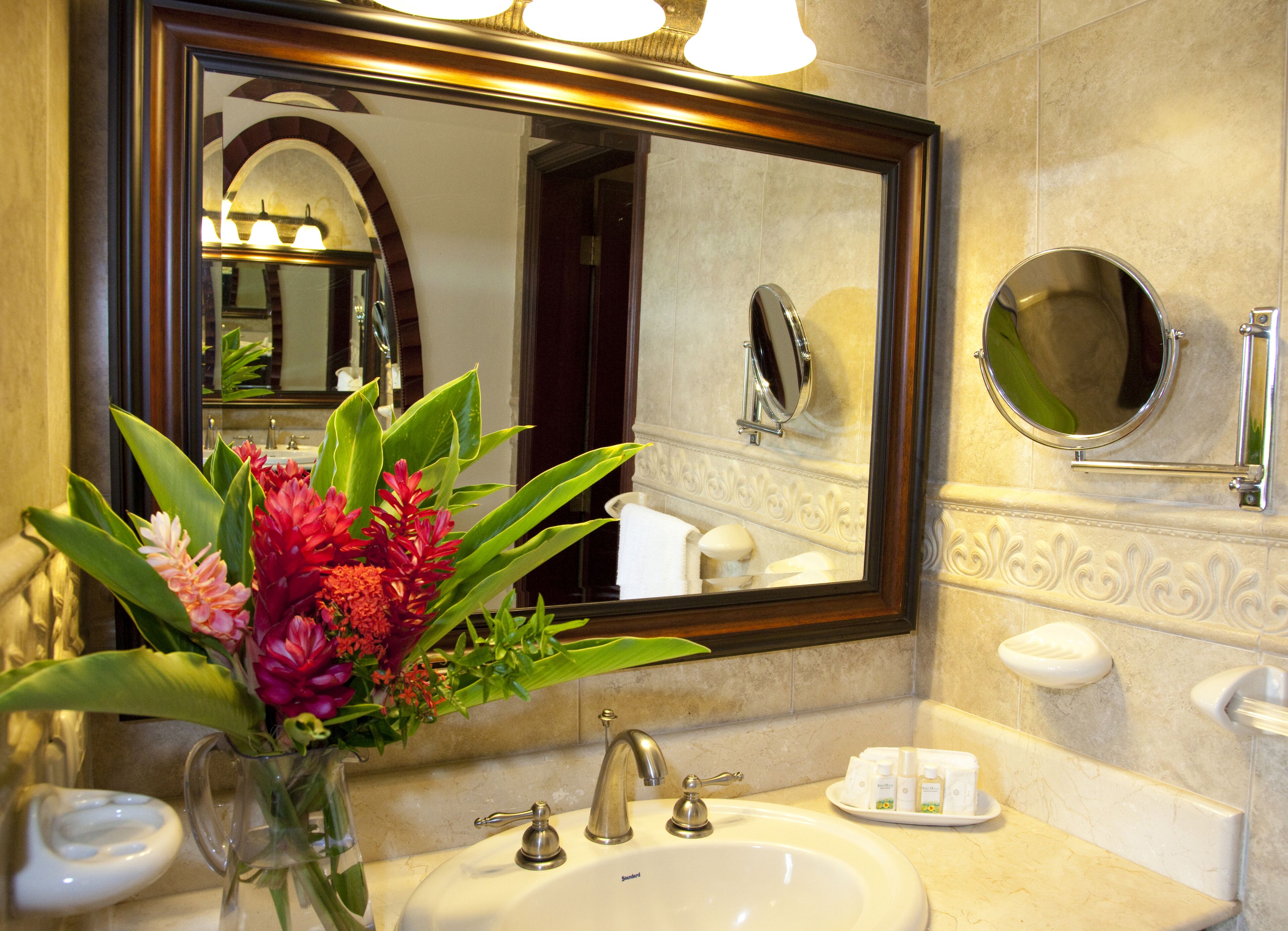 A bathroom with a large mirror, a sink, and a vase of flowers.