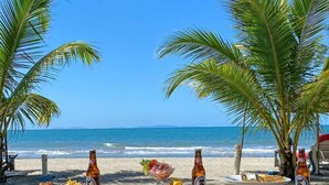 A wooden table set on a beach with drinks and food, palm trees, and the ocean in the background. - La Ensenada Beach Resort - All Inclusive (Tela)
