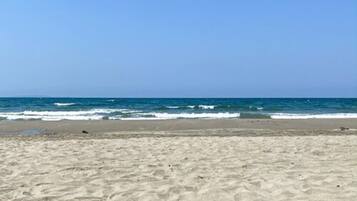 A sandy beach with waves approaching the shore under a clear sky.