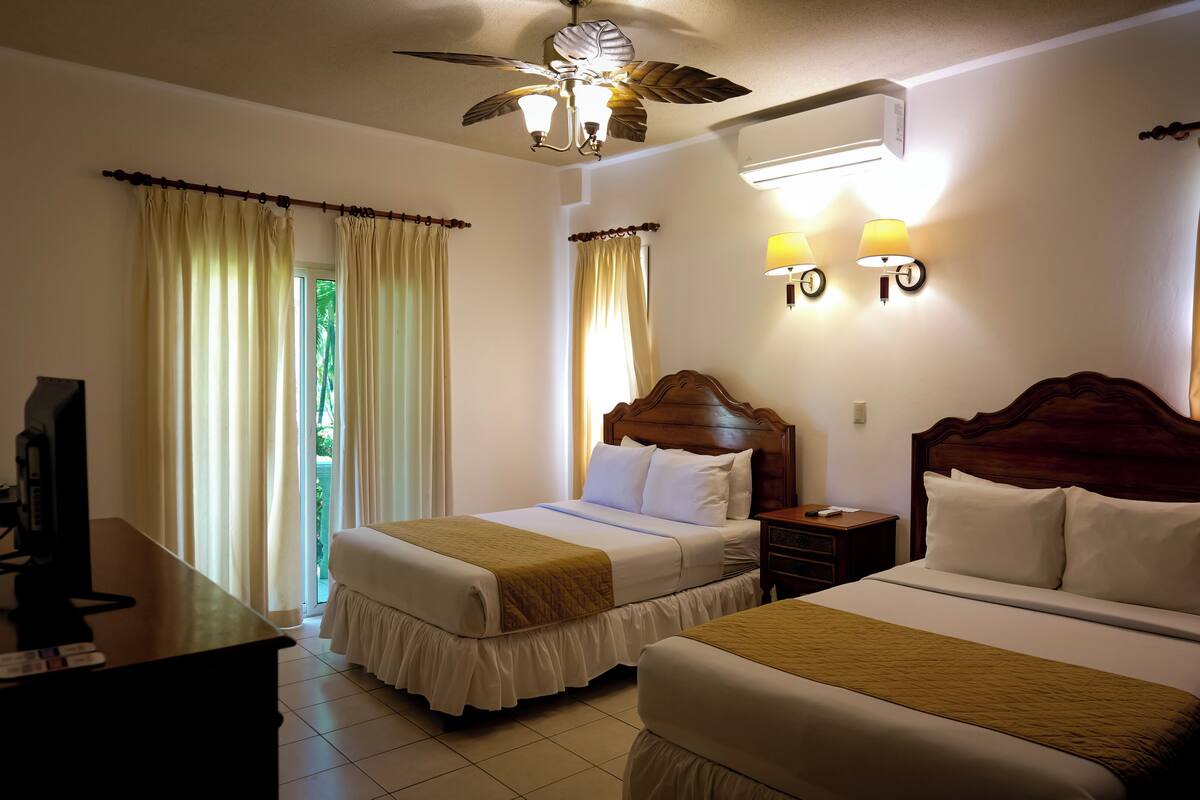 A hotel room with two beds, a desk, a TV, and a ceiling fan.