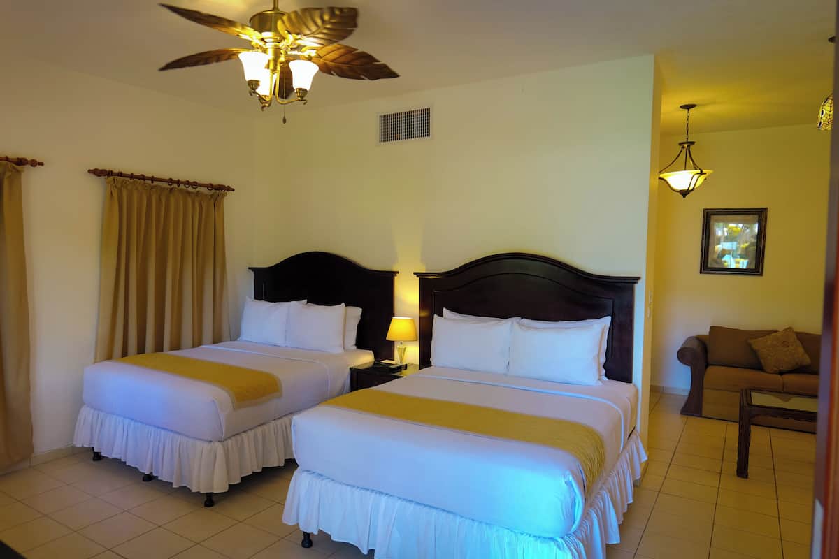 A hotel room with two beds, a ceiling fan, a nightstand, a lamp, a chair, and a window with curtains.