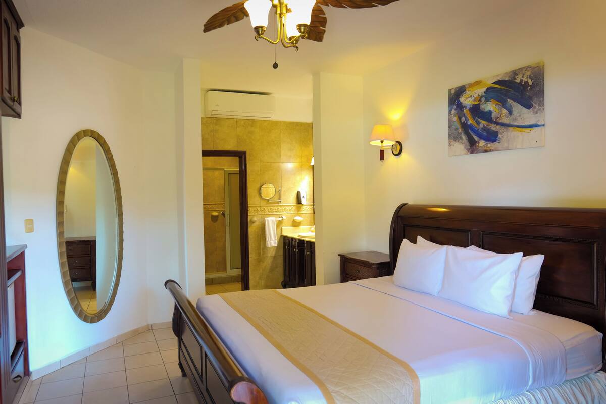 A hotel room with a large bed, a mirror, a dresser, and a painting on the wall.