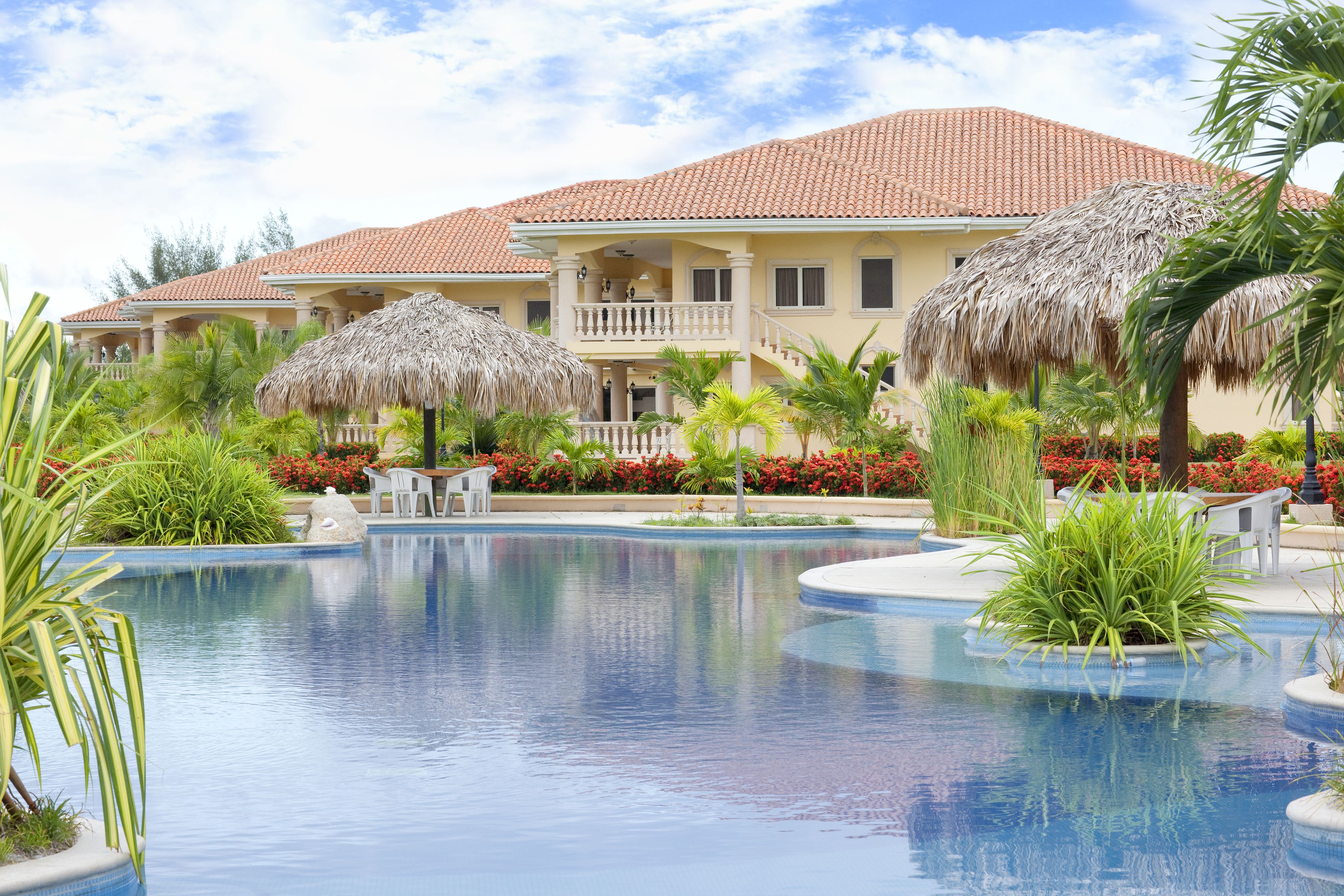 Un resort con piscina, sombrillas de paja y jardines tropicales.