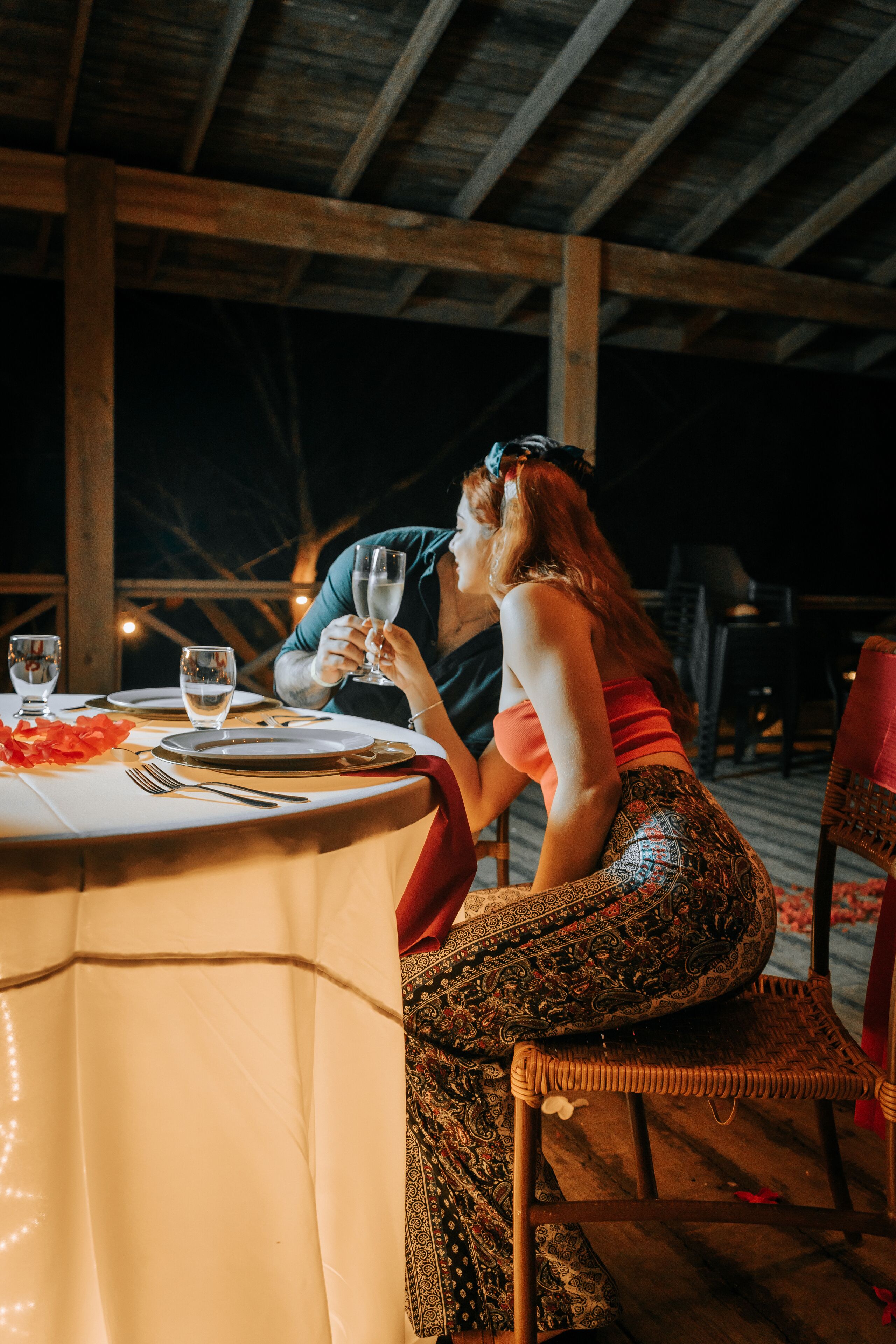 A couple dining at an outdoor table with a white tablecloth, surrounded by wooden beams.