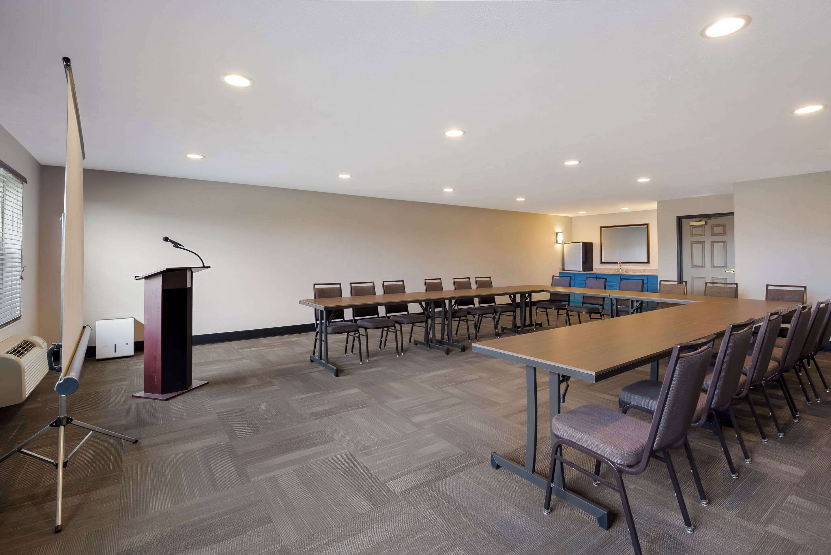 Un salón de conferencias con una larga mesa, sillas, un atril y una pantalla de proyección.