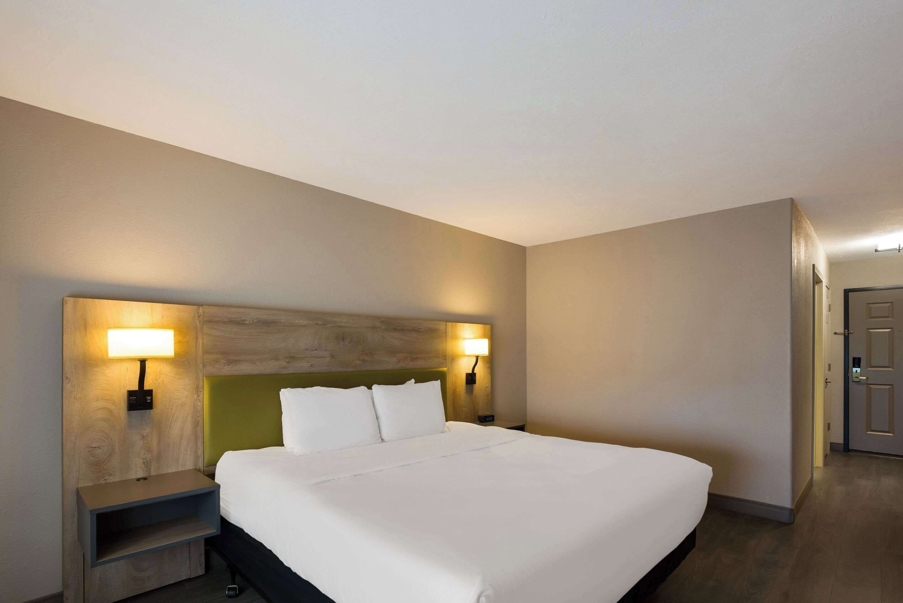 Una habitación de hotel con una cama grande, dos lámparas de noche, una mesita de noche y una puerta.