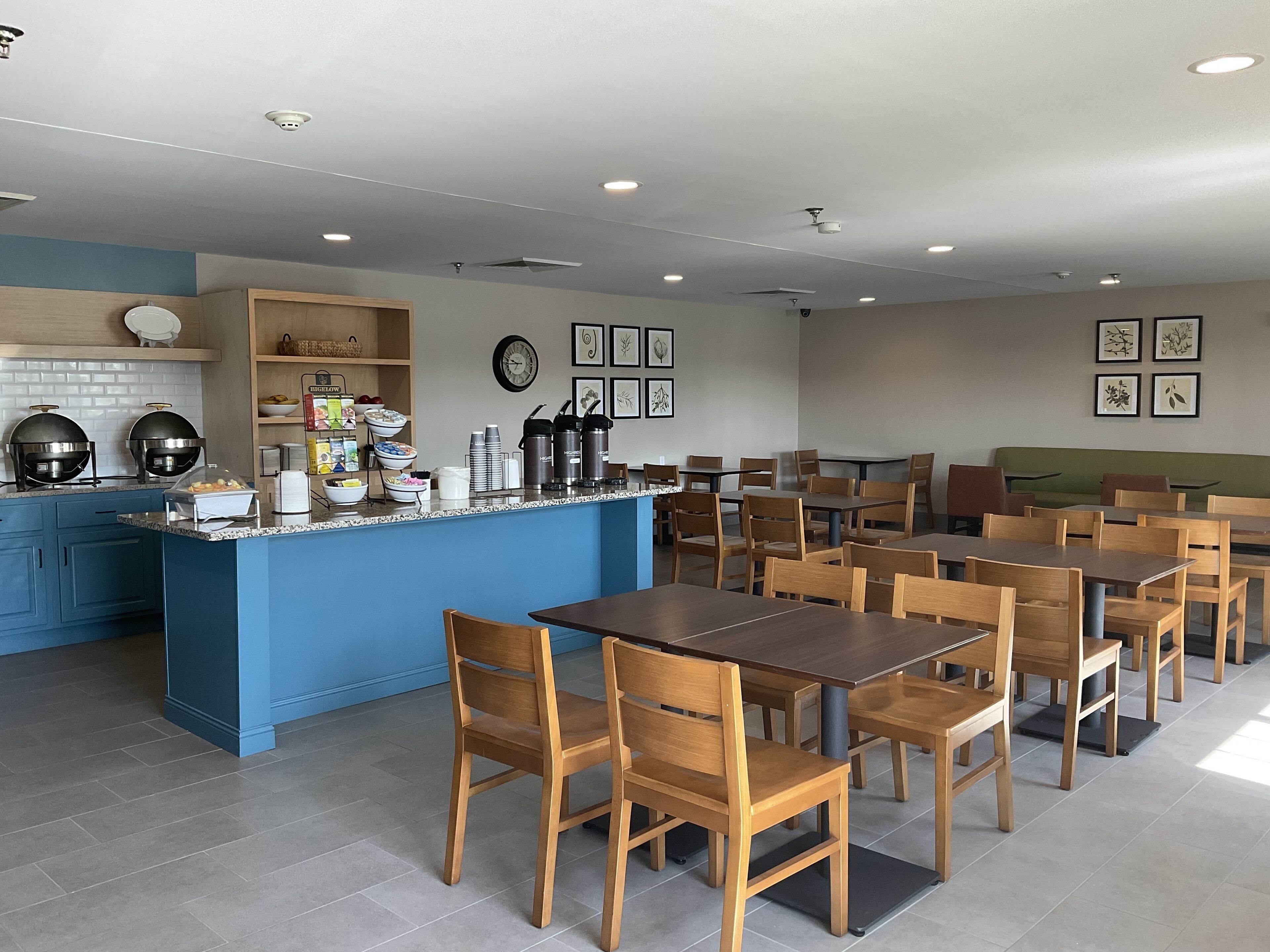 Un comedor moderno con mesas y sillas de madera, una isla central con electrodomésticos de cocina y obras de arte enmarcadas en las paredes.