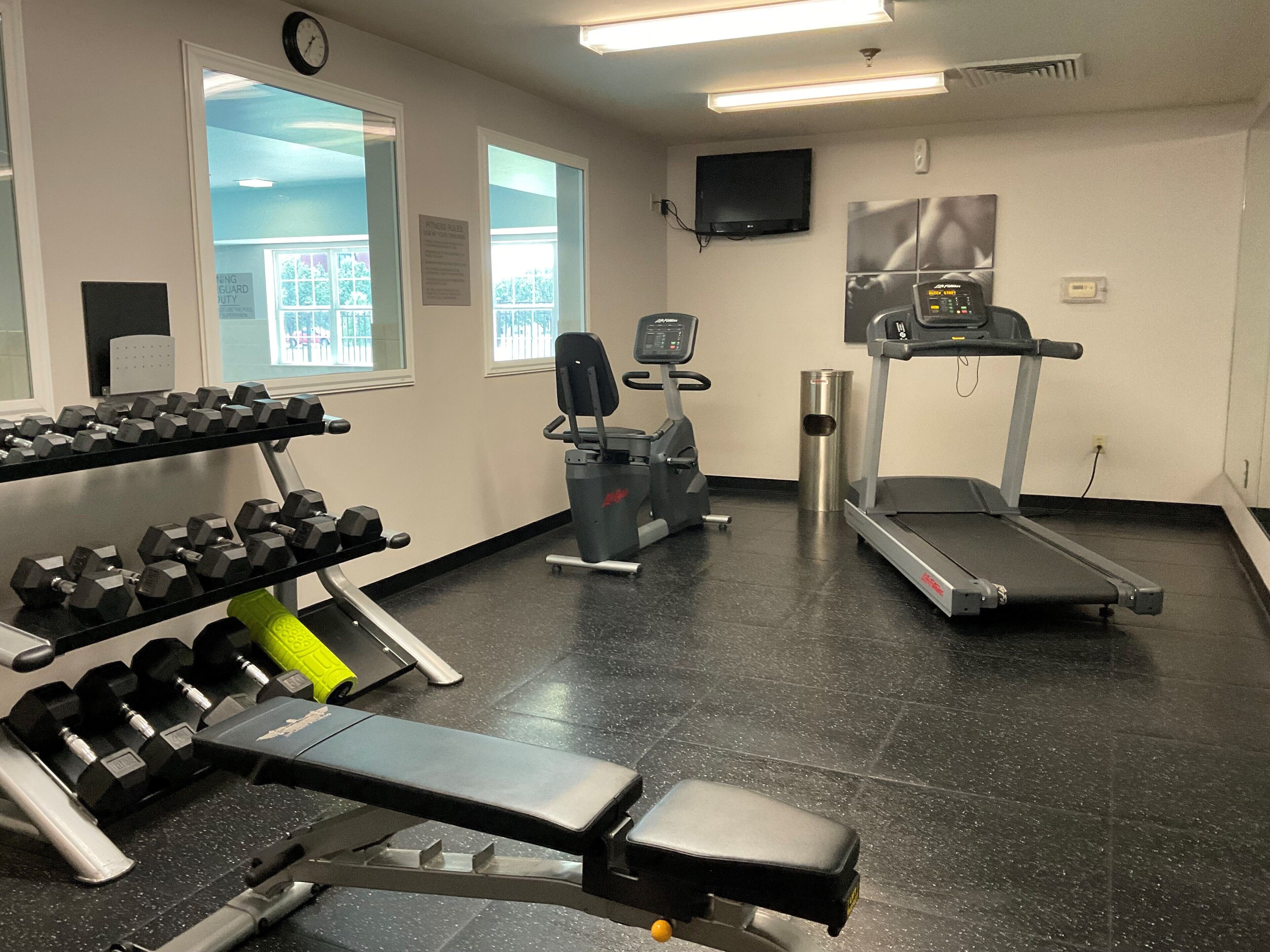 A gym with exercise equipment including dumbbells, a bench, a treadmill, and a stationary bike.
