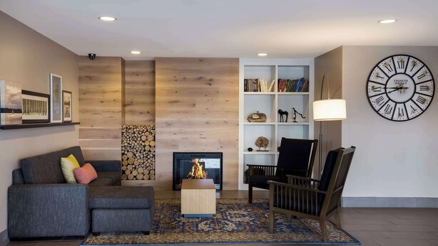 A modern living room with a fireplace, a bookshelf, a large wall clock, and a cozy seating area. - Country Inn & Suites by Radisson, Marion, IL (Marion)