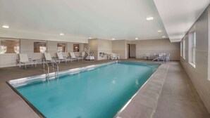 An indoor swimming pool with clear water, surrounded by white lounge chairs and tables, with a high ceiling and natural light from windows. - Country Inn & Suites by Radisson, Marion, IL (Marion)