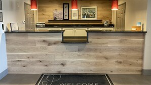 A reception area with a wooden counter, a welcome mat, and framed artwork on the wall. - Country Inn & Suites by Radisson, Marion, IL (Marion)