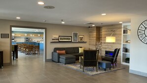 A modern living room with a sofa, coffee table, and a dining area with chairs. - Country Inn & Suites by Radisson, Marion, IL (Marion)