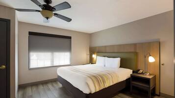 A hotel room with a bed, a nightstand with a lamp, a ceiling fan, and a window with blinds.