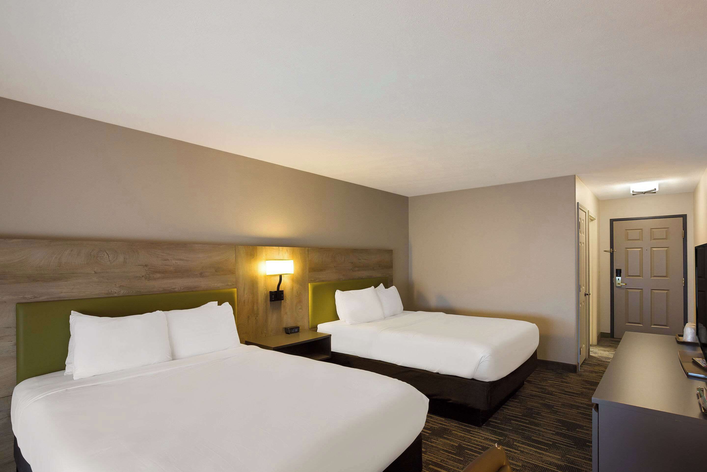 Ein Hotelzimmer mit zwei Betten, einem Schreibtisch, einer Lampe und einer Tür.