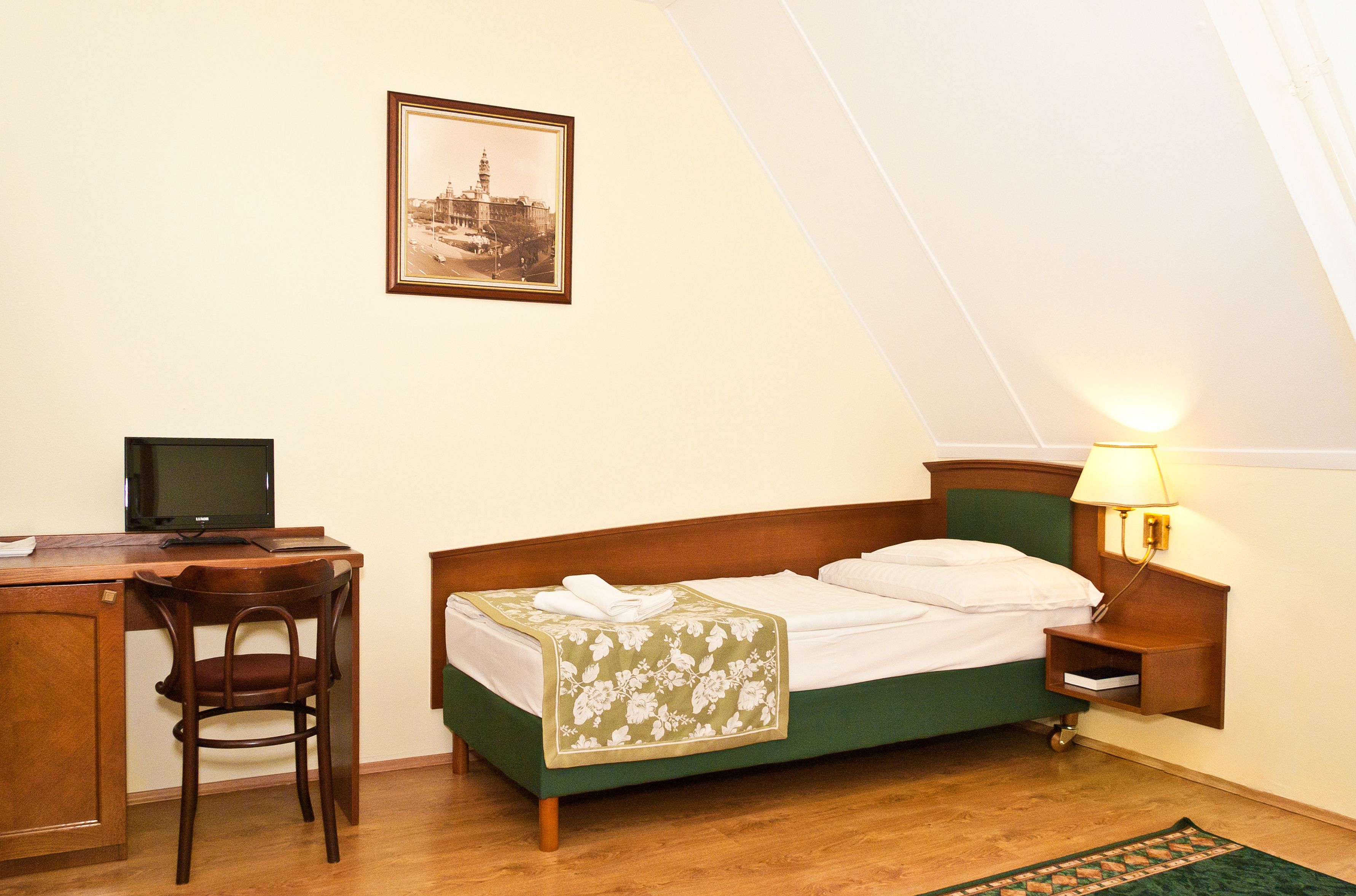 A bedroom with a bed, a desk, a chair, a lamp, and a framed picture on the wall.