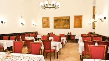 A dining area with tables and chairs, a chandelier, and wall-mounted lights.