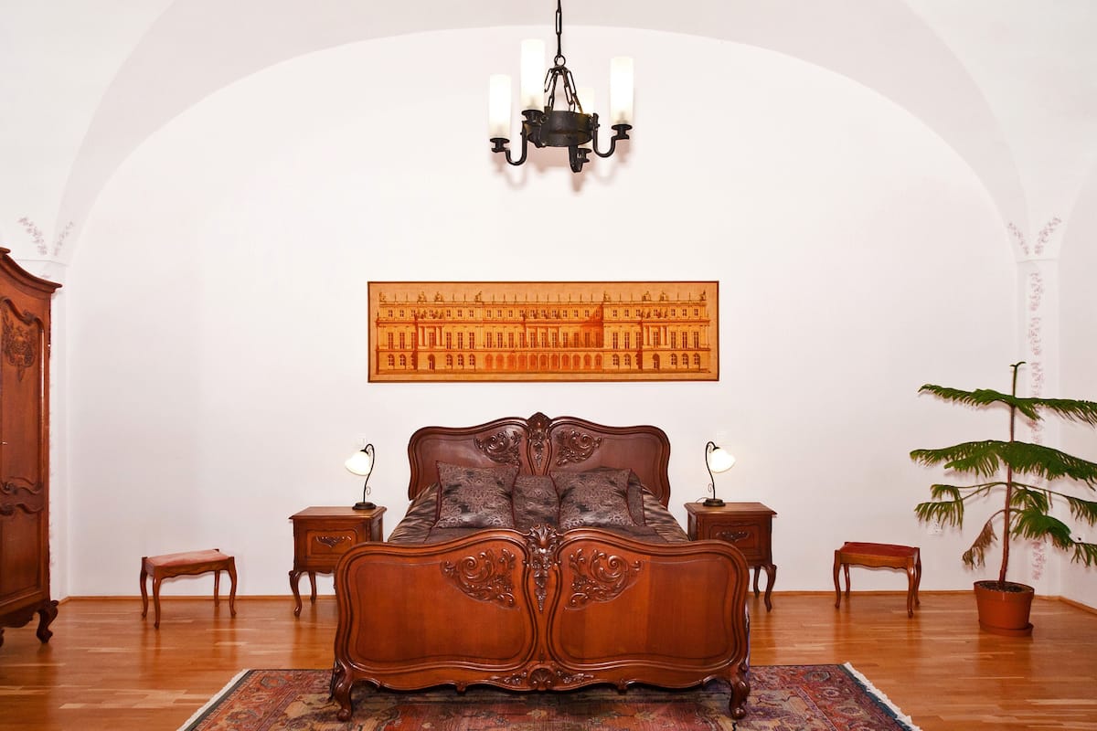 Un dormitorio con una cama grande, muebles de madera, una araña y un cuadro grande en la pared.