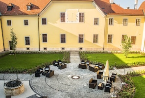 Un patio con mesas al aire libre, una chimenea central y un edificio con varias ventanas y un reloj.