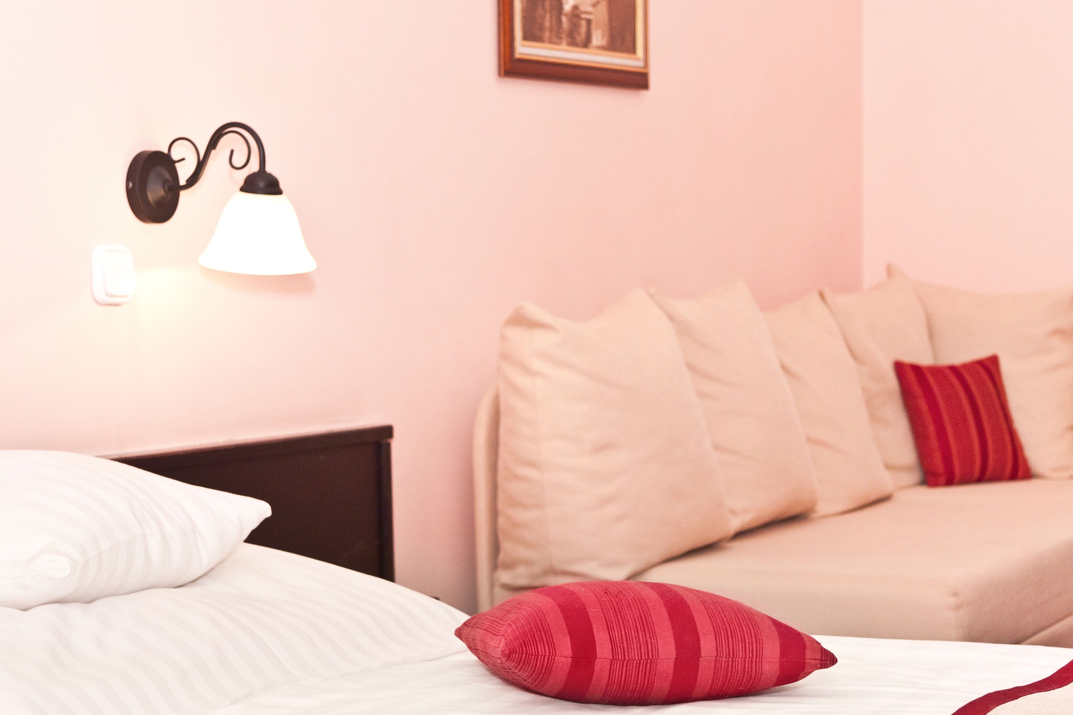 A bedroom with a bed, a nightstand, a wall-mounted lamp, and a sofa with pillows.