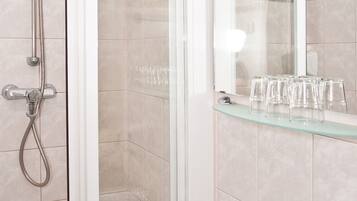 Baño con ducha, lavamanos y repisa de vidrio con vasos.