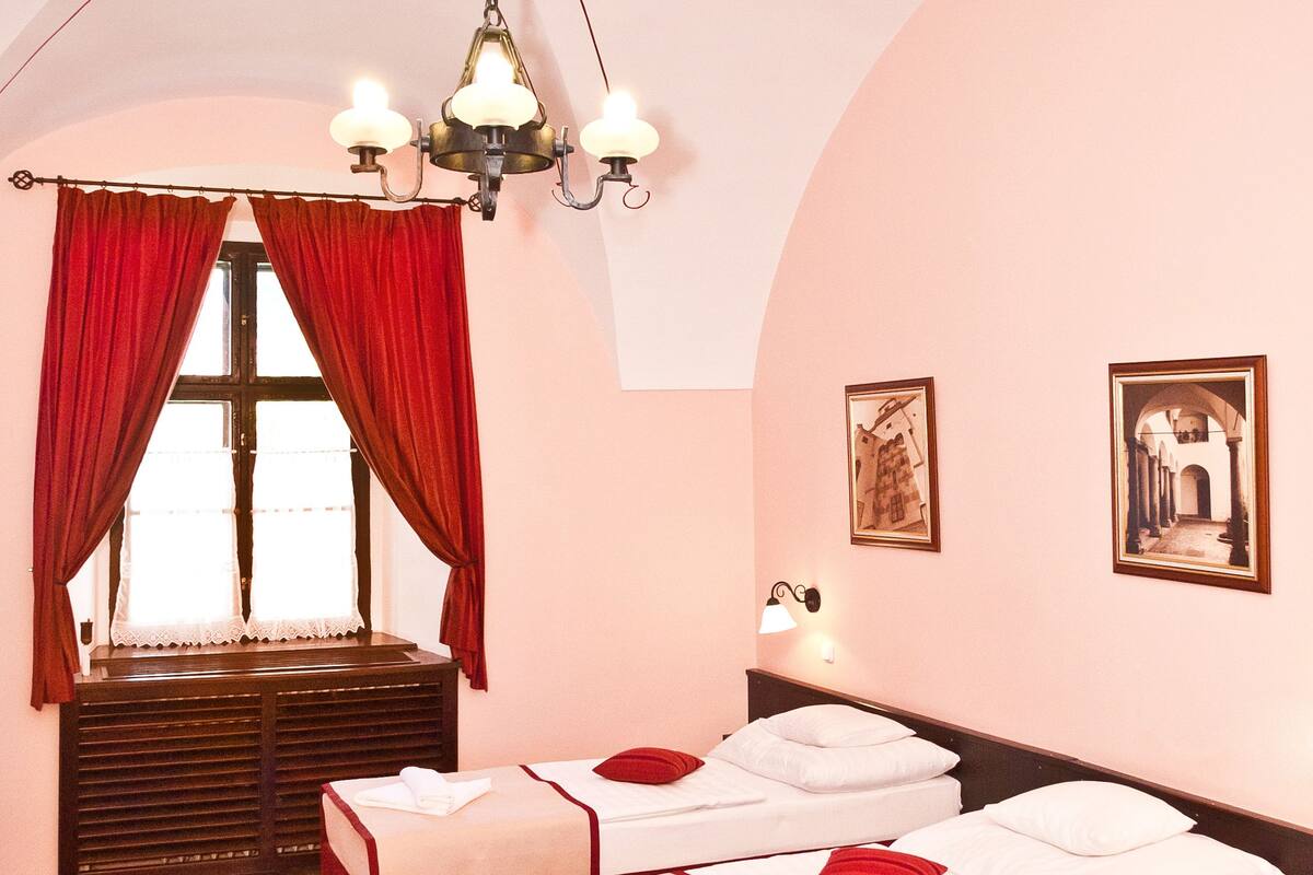 Habitación de hotel con dos camas, alfombra roja, candelabro y dos lámparas de pared.