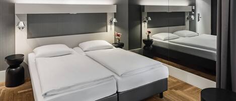 A modern hotel room with a large bed, bedside tables, a mirror, and a wooden floor.