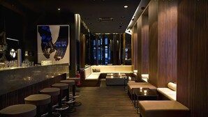 A modern bar area with high stools, a bar counter, and a seating area with sofas and a coffee table. - Hotel AMANO Rooms & Apartments (Berlin)