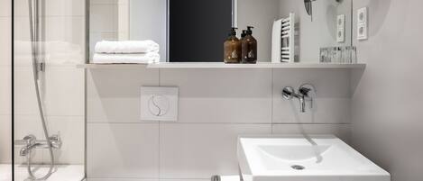 A modern bathroom with a glass shower enclosure, a white sink, and a mirror with a round frame.