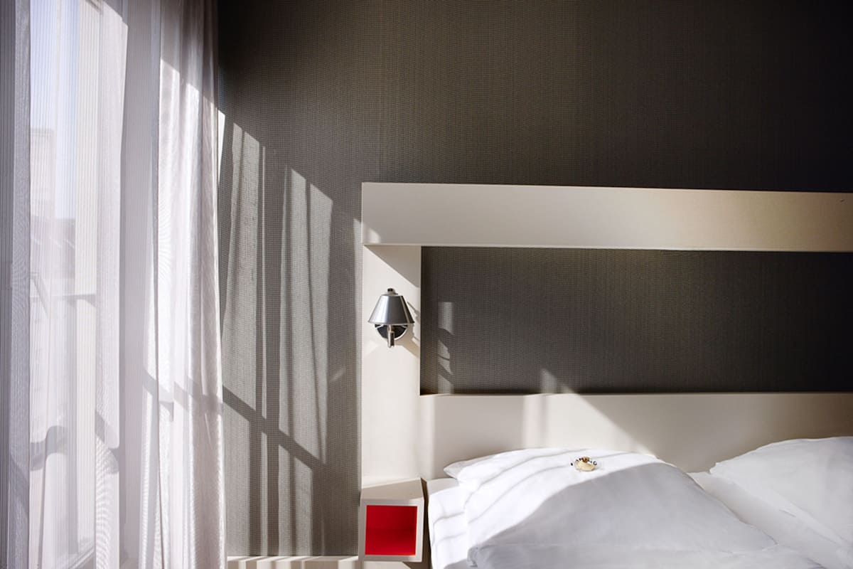 Una habitación de hotel moderna con una cama grande, una mesita de noche y una lámpara de pared.