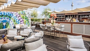 An outdoor seating area with a bar, cushioned chairs, and a mural. - Hotel AMANO Rooms & Apartments (Berlin)