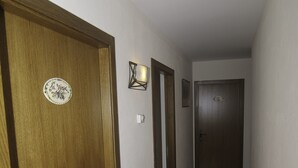 Un pasillo estrecho con puertas de madera, un aplique en la pared y suelo de baldosas.
