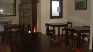 Un comedor con una gran mesa de madera y sillas, un muro de piedra y un ventanal con vistas.