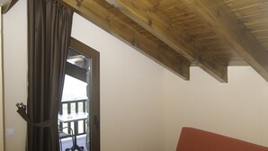 Una habitación con techo de madera, un sofá rojo, una ventana con cortinas y vista a una terraza exterior.