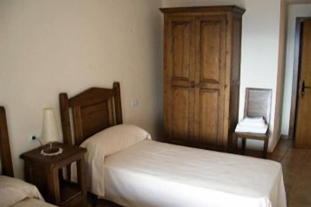 Een slaapkamer met twee eenpersoonsbedden, een houten garderobe en een stoel.