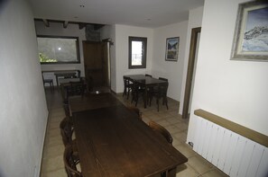 A dining area with a large wooden table and chairs, a window with a view, and a radiator on the wall.