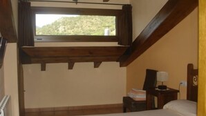 Un dormitorio con techo inclinado, una ventana con cortinas, una cama, una mesita de noche con lámpara y un radiador.
