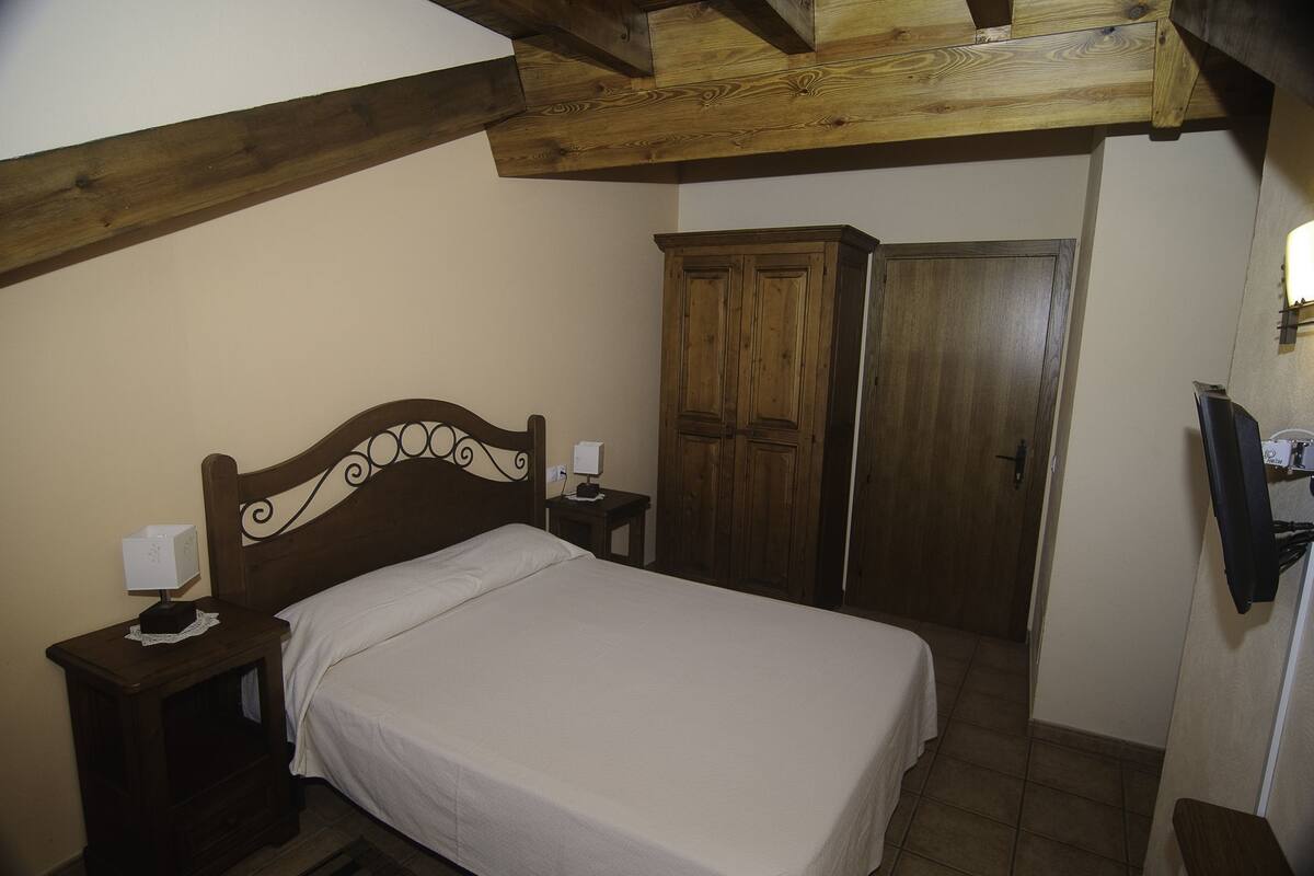 Een slaapkamer met een houten bed, een nachtkastje met een lamp, een kledingkast en een deur.