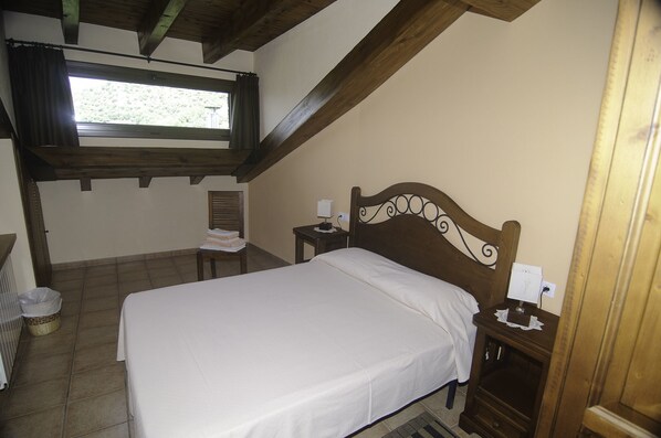 A bedroom with a wooden bed, a nightstand, a chair, a window, and a view of greenery outside.