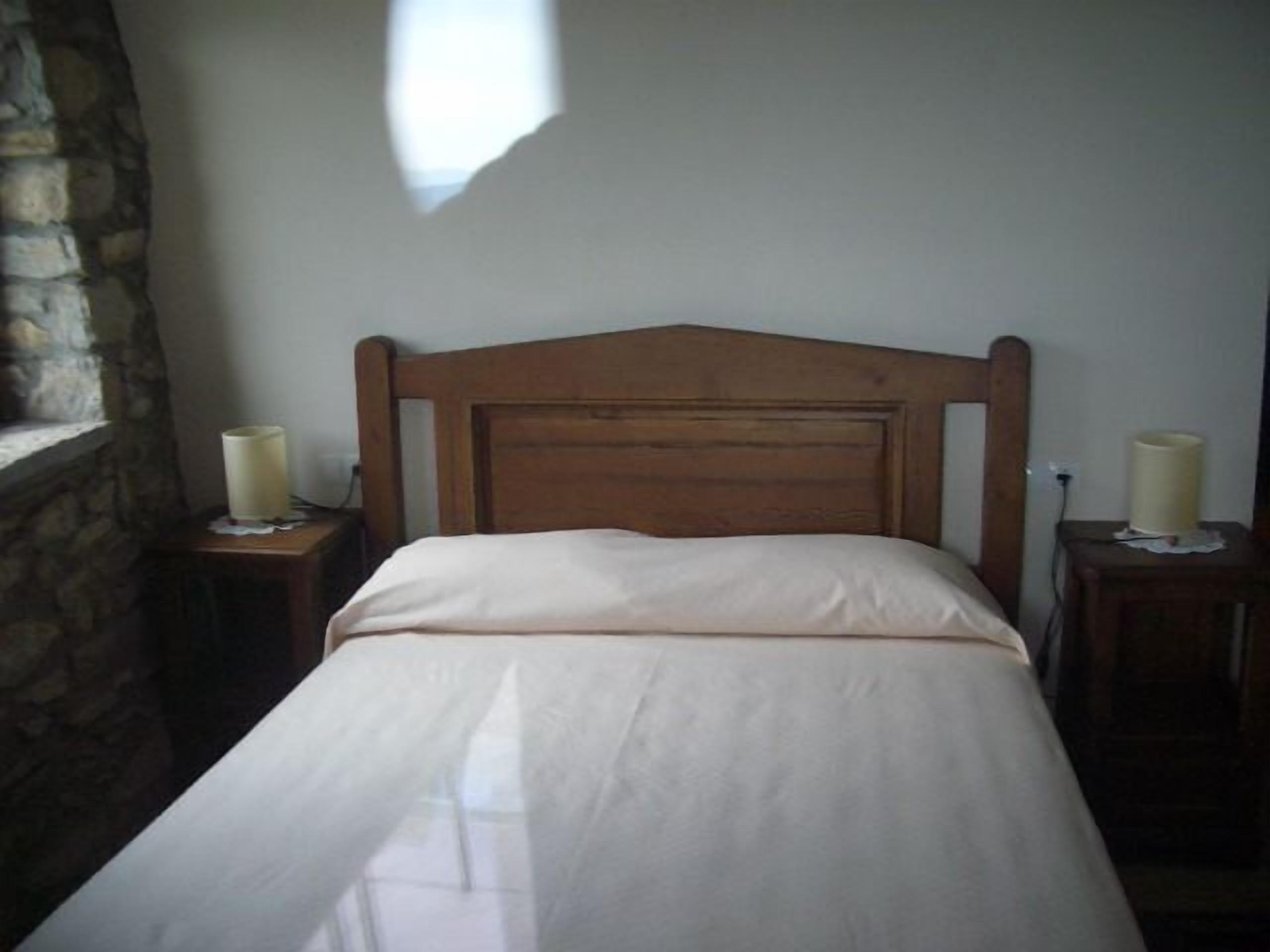 A bedroom with a wooden headboard, a white bedspread, and two bedside lamps on wooden nightstands.