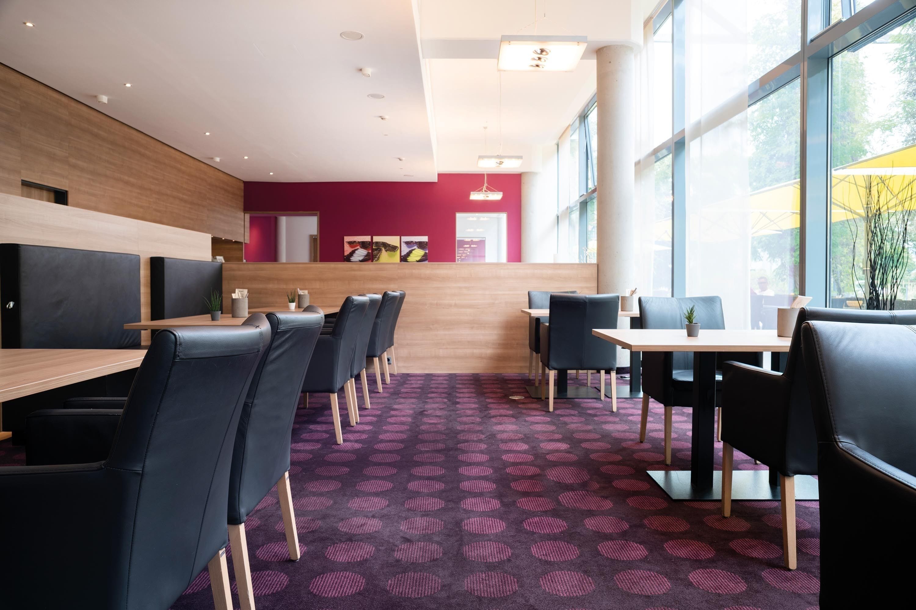 A modern restaurant with a purple patterned carpet, black chairs, and wooden tables.