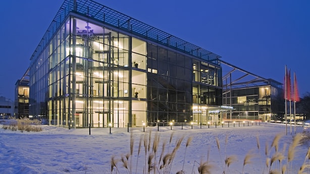 A modern glass building with a snow-covered ground, illuminated by internal lights. - Seminaris CampusHotel Berlin (Berlin)