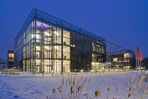 Un edificio moderno de cristal con el suelo cubierto de nieve, iluminado por luces interiores.