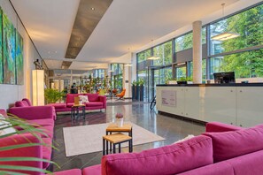 Un hall espacioso con diseño moderno, que cuenta con un mostrador de recepción, zona de estar con sofás y grandes ventanales con vistas a zonas verdes.