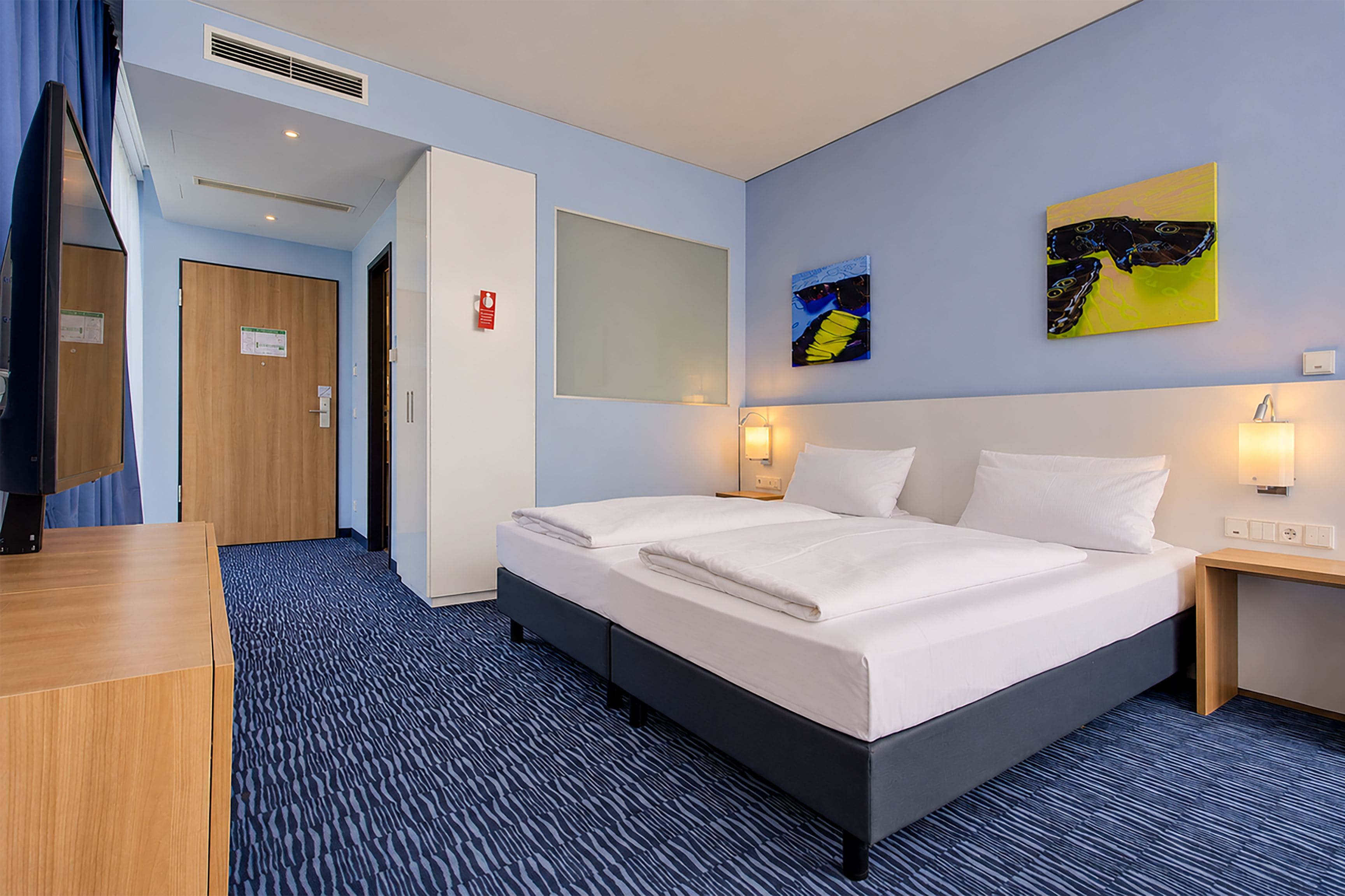 A hotel room with a bed, bedside tables, a desk, and a mirror.