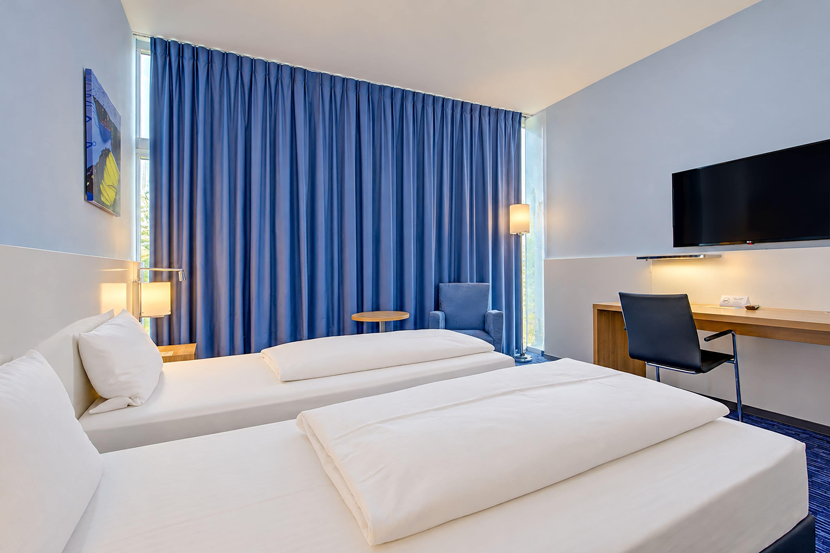 A hotel room with two beds, a desk, a chair, a television, and a window with curtains.